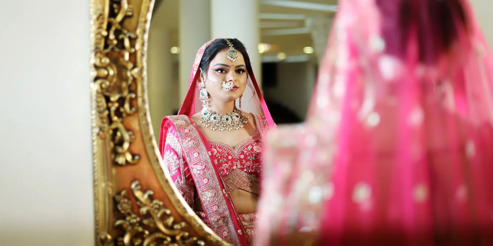 Bride in a red bridal lehenga reflected in an ornate gold mirror